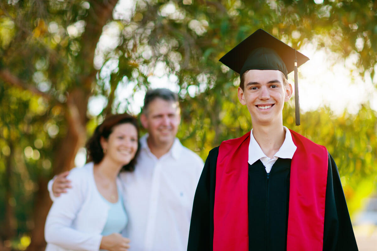 A guy graduate with his parents standing behind them.